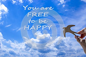 Man hand holding wooden bird on cloud sky background. Words `you are free to be happy`. The development of the imagination, copy