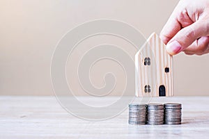 Man hand holding wooden house model over coins stack on table background. Business, Investment, Money Saving, Real Estate and