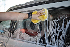 man hand holding yellow sponge cleaning car