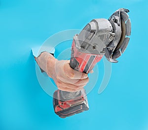 Man hand holds brushless cordless angle grinder that breaks through blue wall