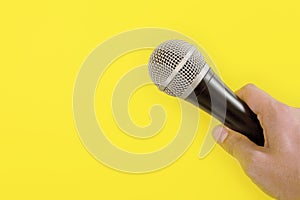 Man hand holds microphone, yellow background, space for text/image left photo