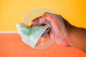Man hand holds surgical mask with yellow and orange background. General personal protective equipment for use in virus diseases