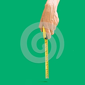 Man hand holds tape measure in inches and centimeters to measure length. Plastic coated steel blade. Hands measuring, Green