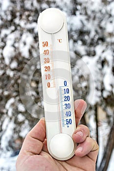 Man hand holds thermometer against trees in winter