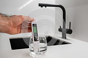 Man hand immerses TDS tester into the water in glass. demonstrates that the water is clean