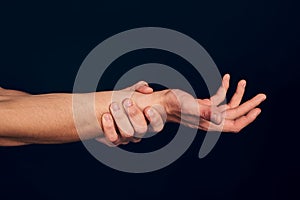 Man hand isolated on dark blue background. Close-up of man holding his wrist. Experiencing wrist pain