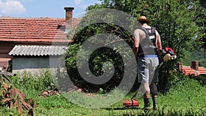 Man with hand lawn mower trimming tall grass in backyard on summer hot day