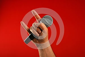 Man hand with microphone and devil horns over red