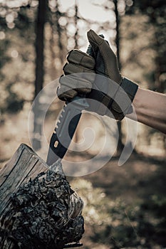 Man hand in a military glove holds a knife in the forest.