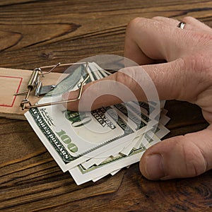 A man hand and a mousetrap with bait money dollars banknotes