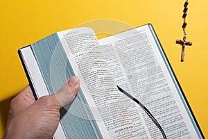 Man hand opening blurred Bible and rosary over yellow