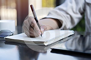 Man hand with pen writing on notebook at coffee shop. Man working in outdoor at coffee shop