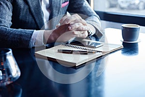 Man hand with pen writing on notebook on table. Man working at coffee shop.