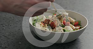 Man hand pick salad with mozzarella, cherry tomatoes and frisee leaves in white bowl on terrazzo surface