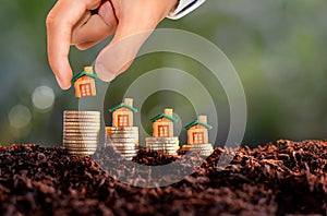Man hand placing house model on stack of coins. Real estate or property development. Construction business investment concept.
