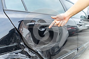 Man hand pointing on car bumper dented broken on black car door photo