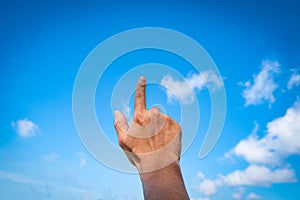 Man hand pointing at something or touching screen on blue sky with cloud background, closeup of hand