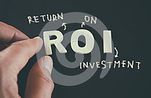 Man hand pointing at the words ROI Return On Investment written on black leather background photo