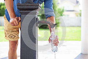 A man hand pours water from a tap from a drinking column into a plastic bottle. Ð¡ity water tap with drinkable water in park. col