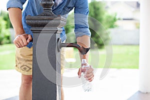 A man hand pours water from a tap from a drinking column into a plastic bottle. Ð¡ity water tap with drinkable water in park. col