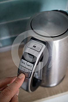 Man hand click on the button iron electric kettle on the background of the kitchen