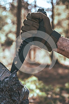 Man hand in a protective glove holds a knife in the forest.