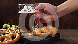 Man hand puts back a mug of light beer on a dark wooden table.
