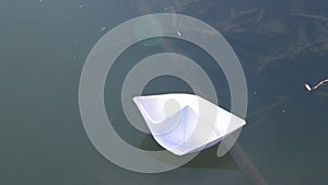 Man hand puts small white paper boat floating on smooth lake, river water in afternoon. Origami ship Sailing. The