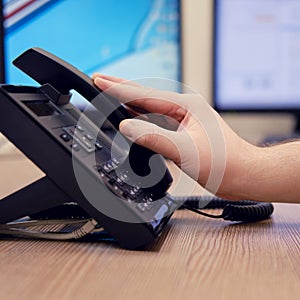 A man hand puts a telephone receiver at the monitors of office computers. Ending a telephone conversation at the workplace, table