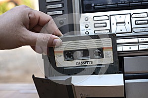 Man hand putting cassette into old fashioned audio tape player on desk wood background