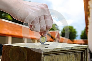A man hand putting coin into a wooden box as donation.