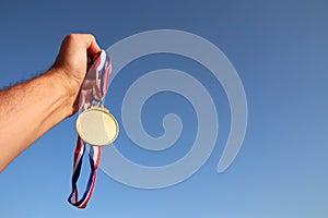 Man hand raised, holding empty gold medal against sky. award and victory concept. For mock up.