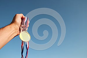 Man hand raised, holding empty gold medal against sky. award and victory concept. For mock up.
