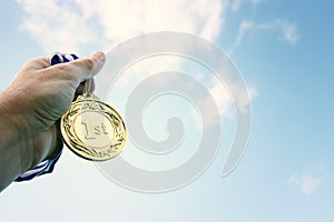 man hand raised, holding gold medal against sky. award and victory concept