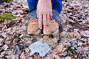 A man hand reaches for a dirty discarded medical mask on the ground