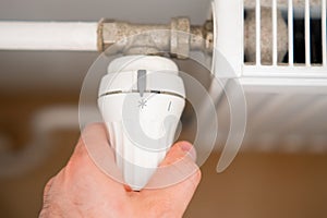 Man hand regulates temperature knob of heating radiator to reduce heating costs.