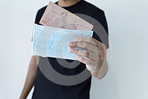 Man hand`s holding medical protective mask and cash thai bath. Concept mask expensive