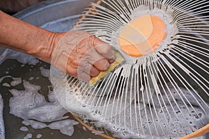 Man hand scrubbing a dirty fan components in the basin with a detergent
