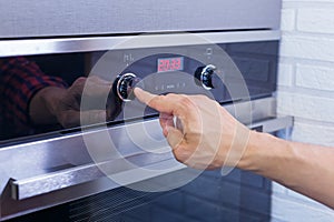 Man hand setting cooking mode on electrical oven. Male finger press button on control panel on oven, close up