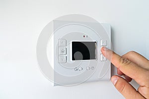 Man hand setting the room temperature on a modern programmable thermostat water heater boiler. Smart home.