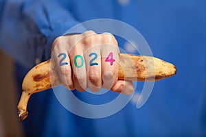 Man hand in shirt holds banana. Numbers 2024 on fingers