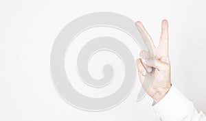 Man hand shows victory gesture, point number two on white wall background