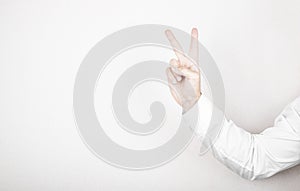 Man hand shows victory gesture, point number two on white wall background