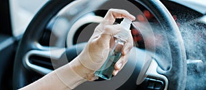 Man hand spraying alcohol sanitizer on steering wheel in his car, against Novel coronavirus or Corona Virus Disease Covid-19.