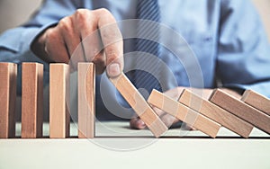 Man hand stopping a falling domino effect of risk.