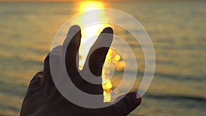 Man hand at sunset on sea, ocean beach. A man`s hand in sun`s rays on background sea water in nature. Glare of evening