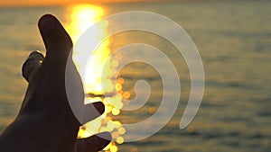 Man hand at sunset on sea, ocean beach. A man`s hand in sun`s rays on background sea water in nature. Glare of evening