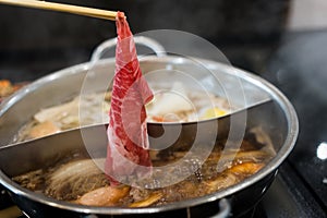 Man hand takes raw delicious beef sliced put cooking in hot boiled soup