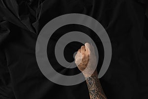Man hand with tattoos holding wrinkle black fabric texture