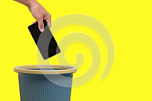 Man hand throws cell phone into trash can on yellow background